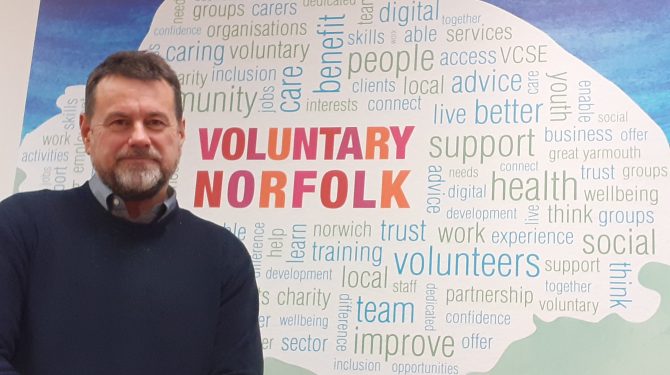 Alan Hopley in front of Voluntary Norfolk logo