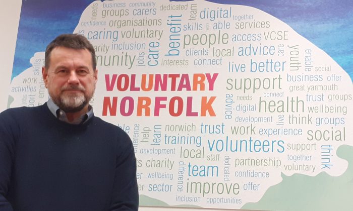Alan Hopley in front of Voluntary Norfolk logo