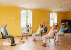 people with arms above their heads sitting down, taking part in chair yoga